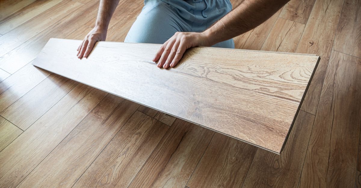 A man stands on a hardwood floor, holding a wooden plank in both hands, focused on his task.
