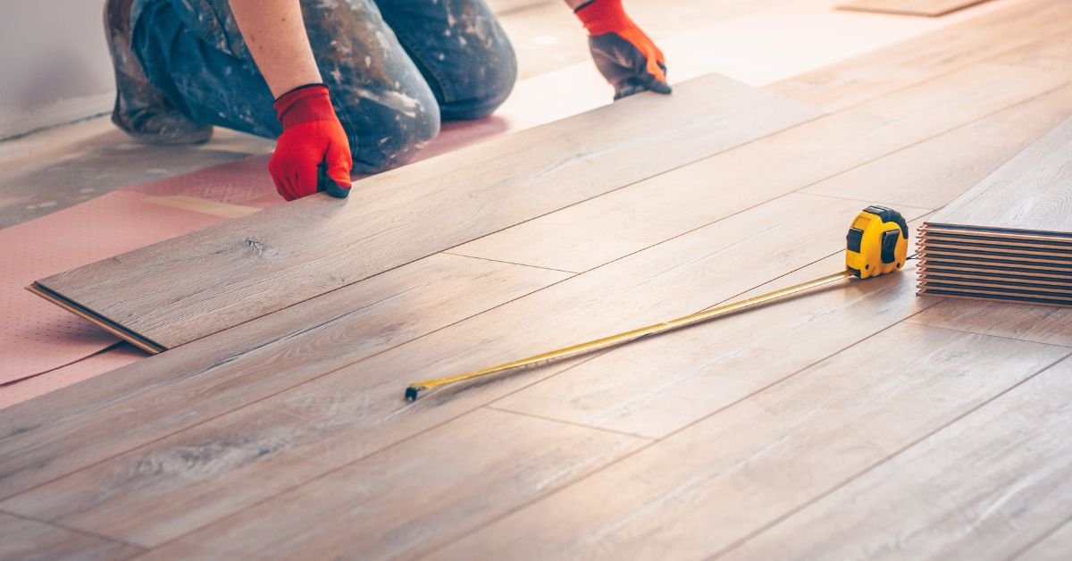 A person installing luxury vinyl  floorboards, kneeling on the ground with tools and planks around them.