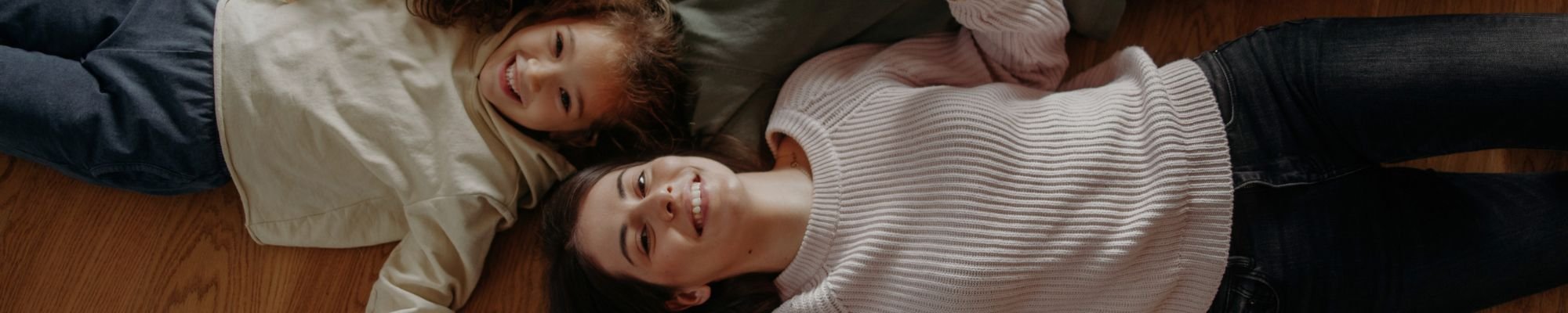 Family lying on the floor together, smiling and enjoying each other's company in a relaxed setting.