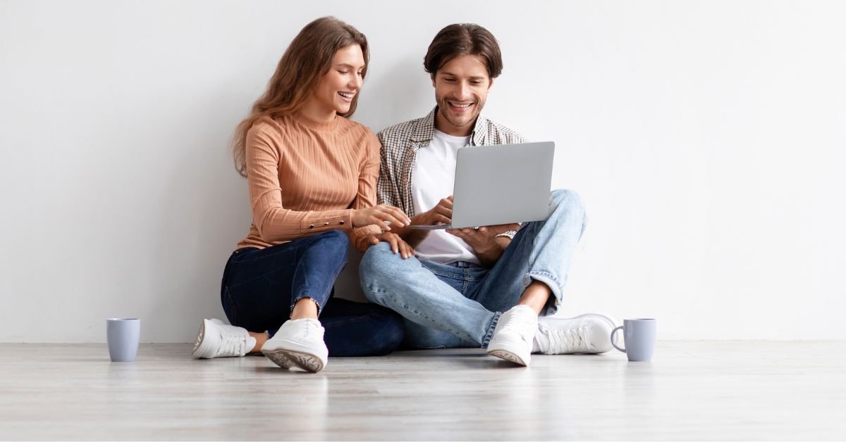 A couple sitting on the floor, focused on a laptop, sharing ideas and enjoying each other's company.