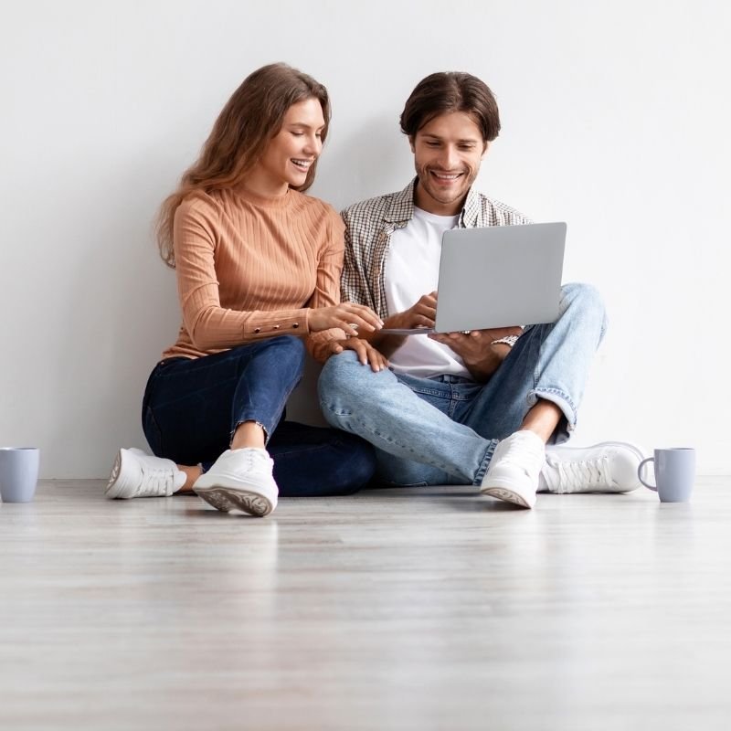 A couple sitting on the floor, focused on a laptop, sharing ideas and enjoying each other's company.