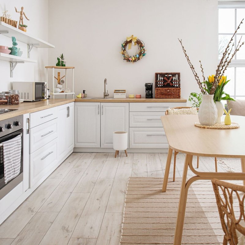 A bright white kitchen featuring wooden floors and a wooden table, creating a warm and inviting atmosphere.
