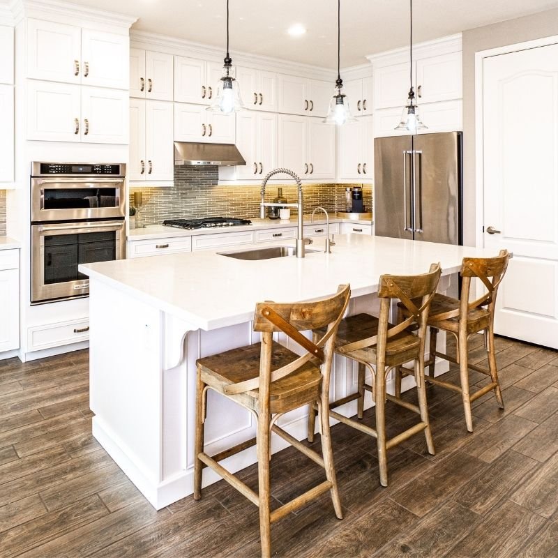 A modern kitchen featuring white cabinets and warm wooden floors, creating a bright and inviting atmosphere.