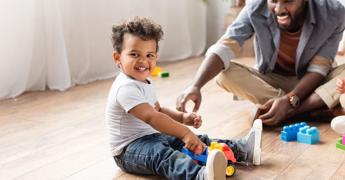 A man and a child are playing together on the floor with colorful toys scattered around them.