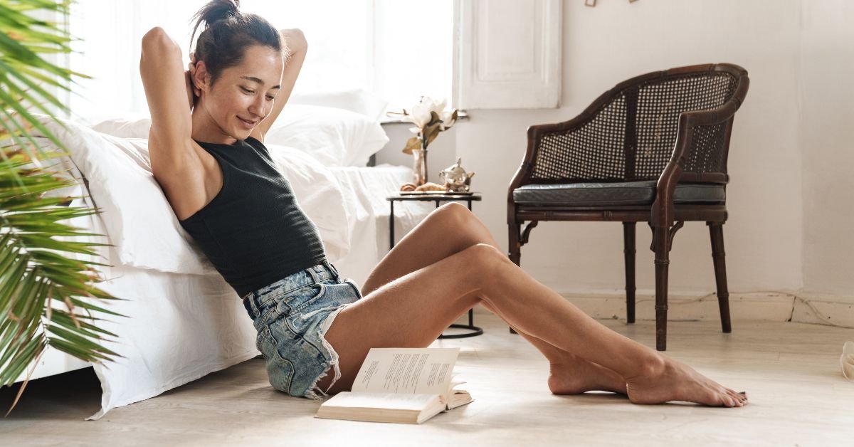 A woman is seated on the floor, legs bent and raised, creating a casual and comfortable atmosphere.