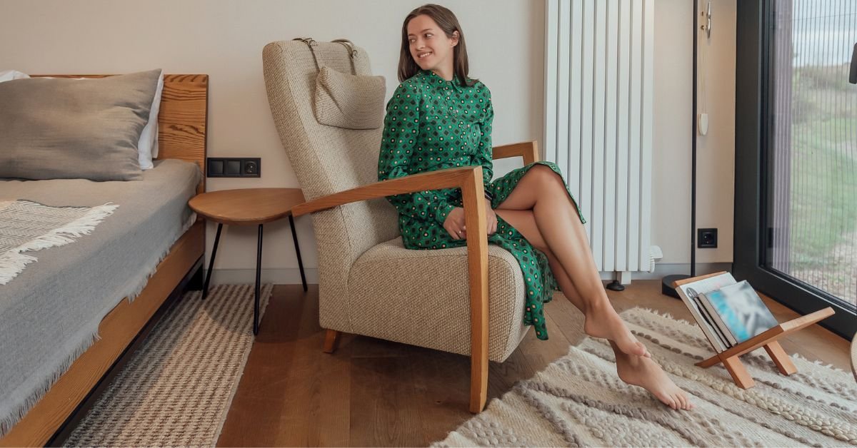 A woman sitting in a chair, gazing out of a window, with soft light illuminating the room.
