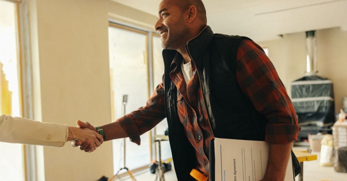 a  man and woman shaking hands inside a cozy home, symbolizing agreement or partnership.
