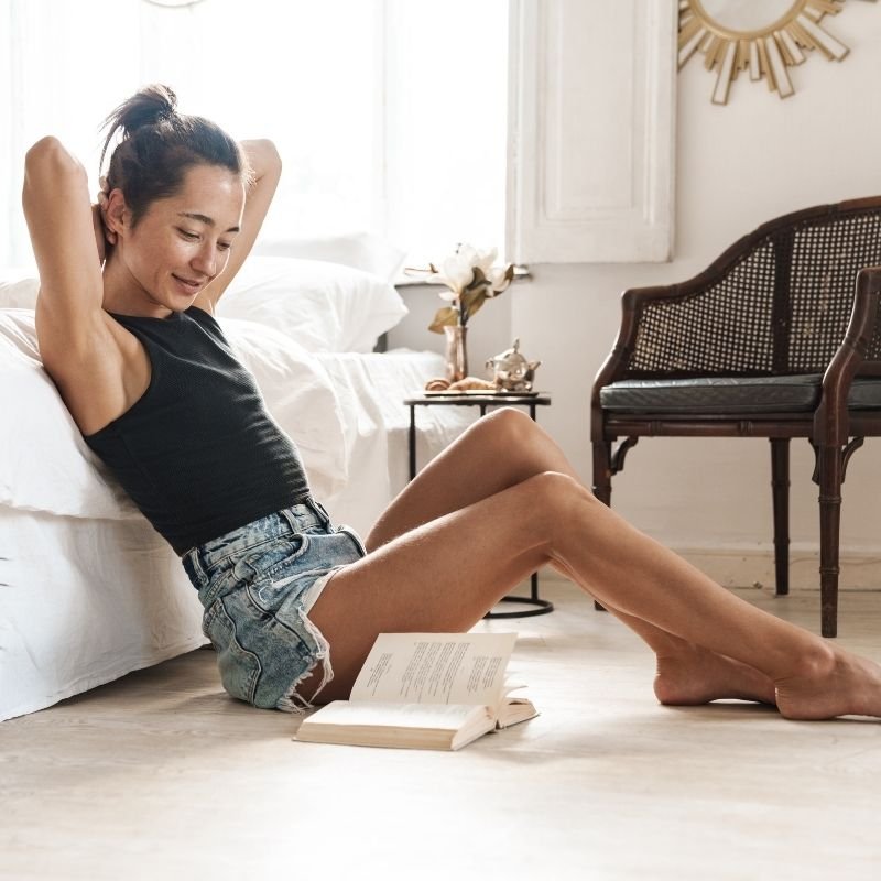 A woman sitting cross-legged on the floor, engrossed in reading a book
