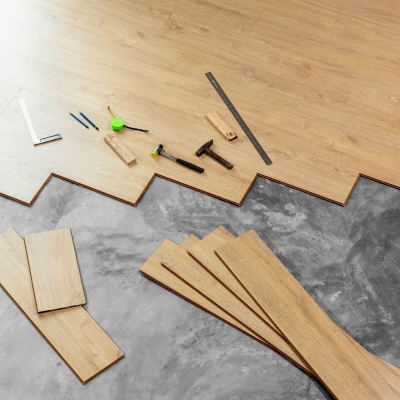 A floor covered with various tools and pieces of wood flooring, indicating a woodworking or renovation project in progress.