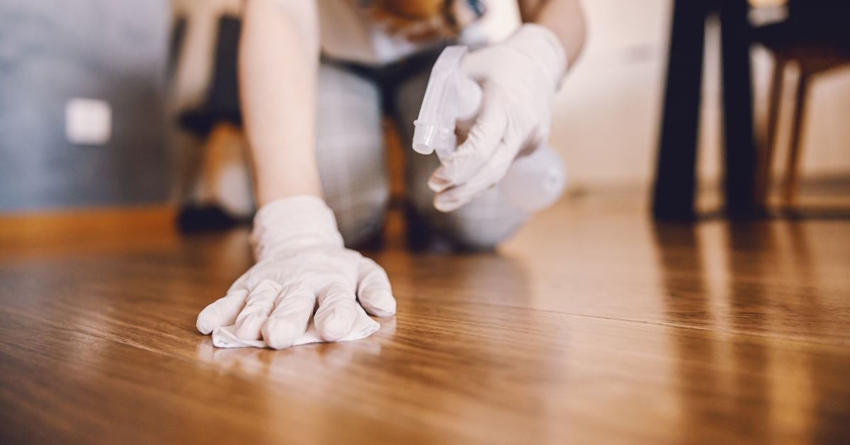 A person in gloves scrubbing a wooden floor, focused on cleaning and maintaining its shine and appearance.